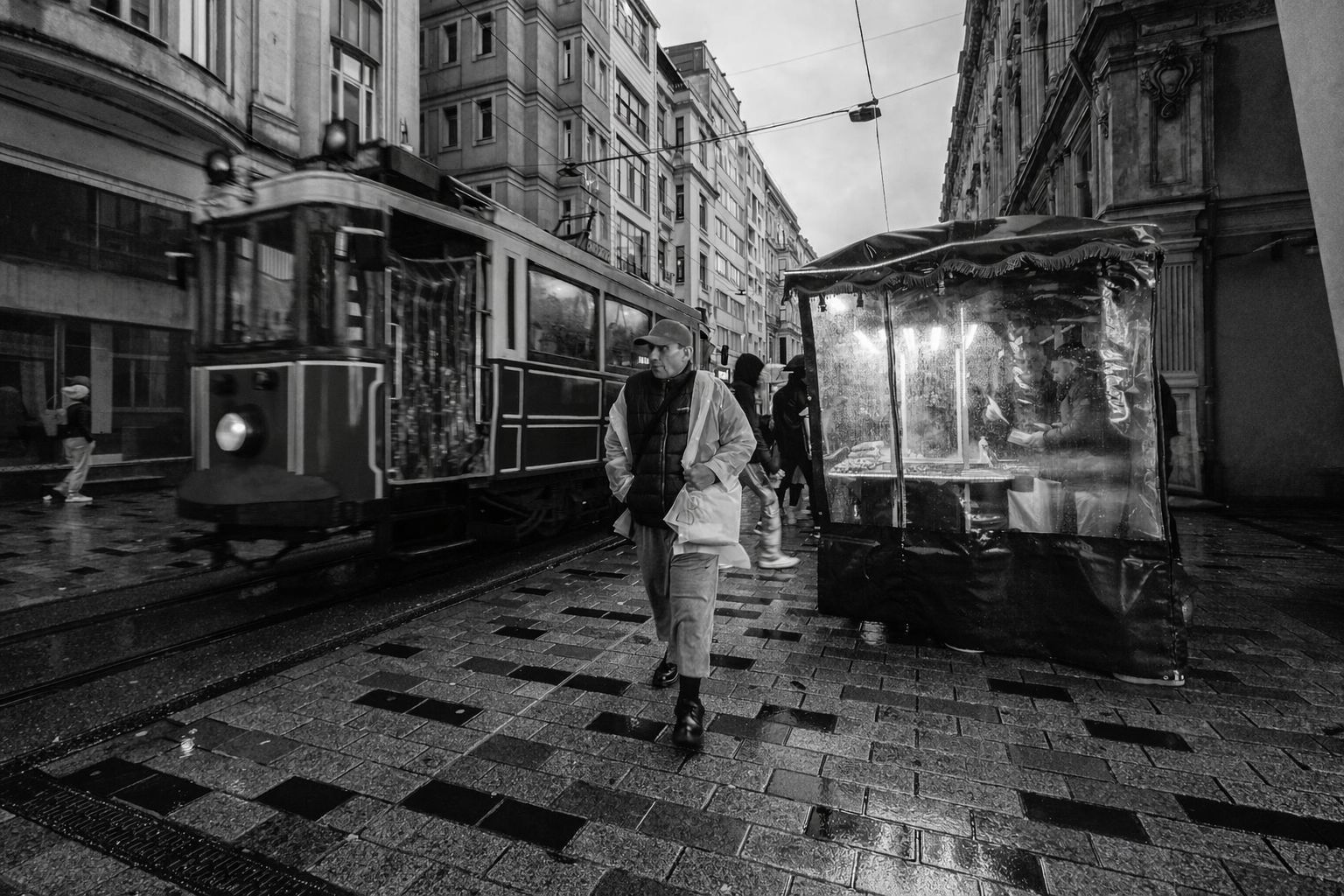 Svartvit gata med spårvagn, människor och försäljningsstånd i stadsbild.